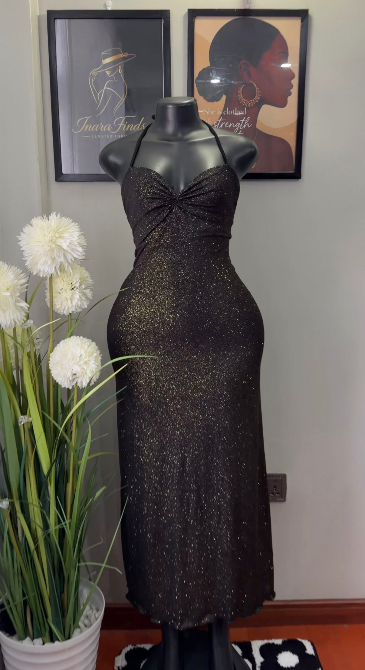 A sleeveless black halter-neck dress with a textured, glittery shimmer, displayed on a black mannequin. The dress features a sweetheart neckline with a twisted bow detail at the bust and a fitted silhouette.