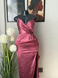 A dusty rose satin wrap dress displayed on a black mannequin torso, styled with white flowers in the foreground and framed art on a light wall background.